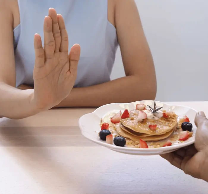 A hand raised to decline a plate of food, illustrating appetite awareness