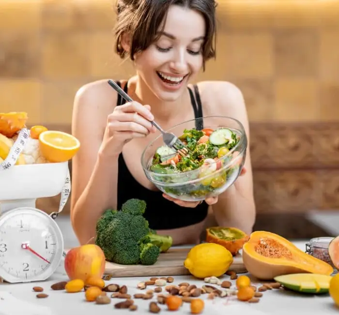 A person eating a fresh salad surrounded by vegetables and fruit